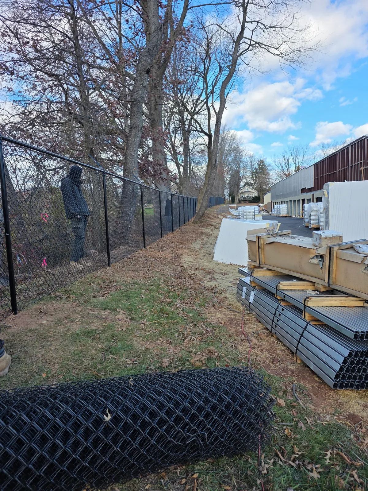 Black vinyl-coated chain link fence with materials staged for commercial installation